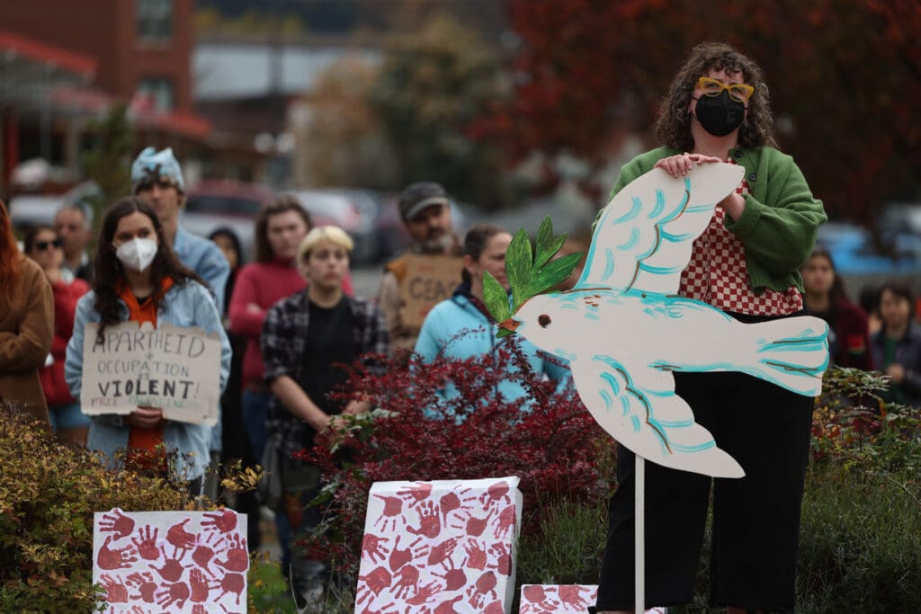 A supporter holds a sign shaped and painted to look like a white dove as many others hold up signs behind them.