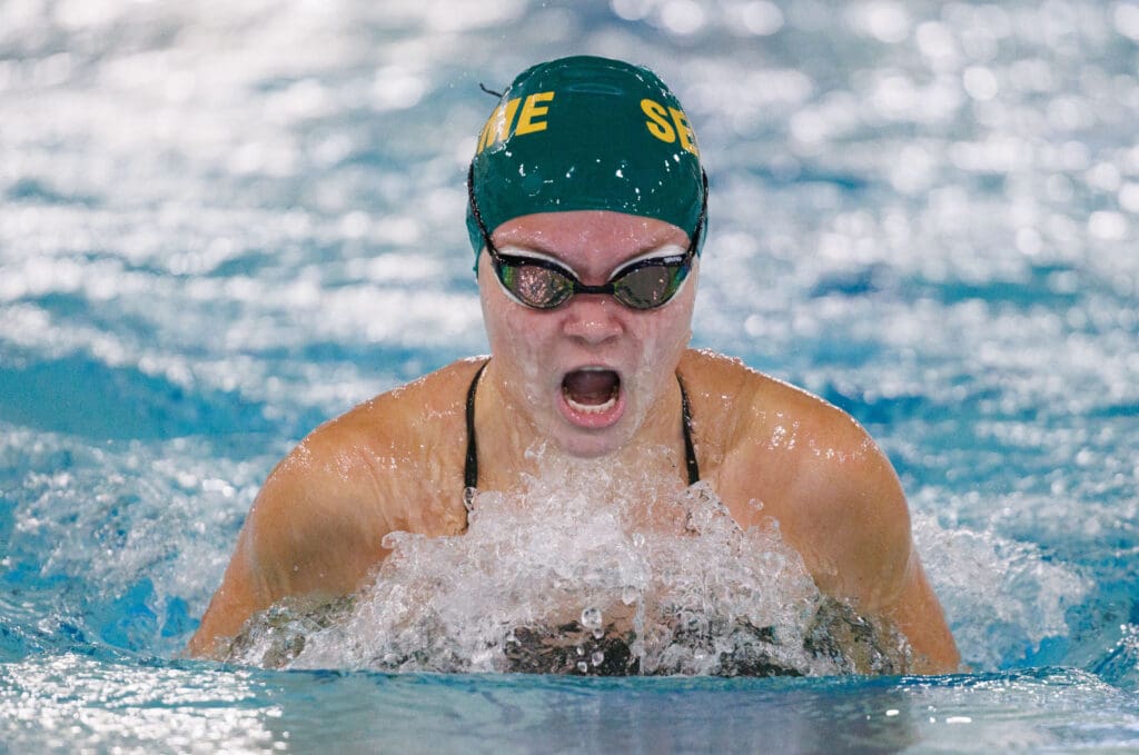 Kateryna Isakova competes in the 100-yard breaststroke as she breaches from the water with an intense expression.