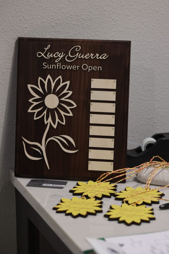 A plaque and awards in honor of Lucy Guerra sit on a reception desk at Bellingham Training and Tennis Club next to their signature yellow flowers.