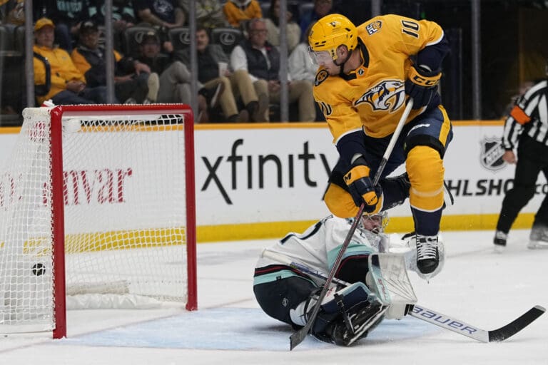 Nashville Predators center Colton Sissons (10) leaps over Seattle Kraken goaltender as spectators react from behind the clear barriers.