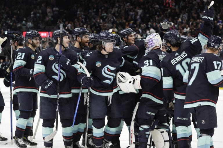 Seattle Kraken players celebrate in a close crowded huddle on the ice rink.