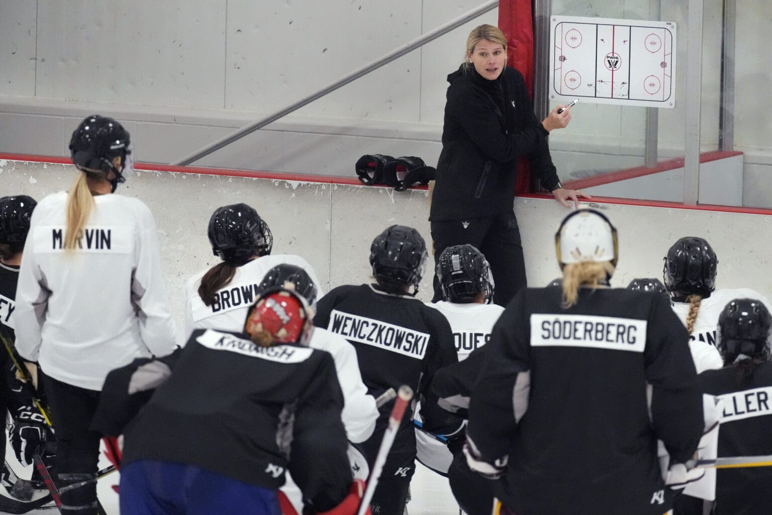 Courtney Kessel, head coach of the Boston-based team of the Professional Women's Hockey League, instructs her players during a practice as she sits on the sideline barrier.