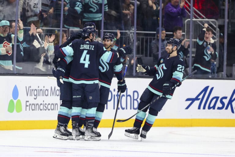 The Seattle Kraken celebrate a goal as they give each other high fives in a close huddle.