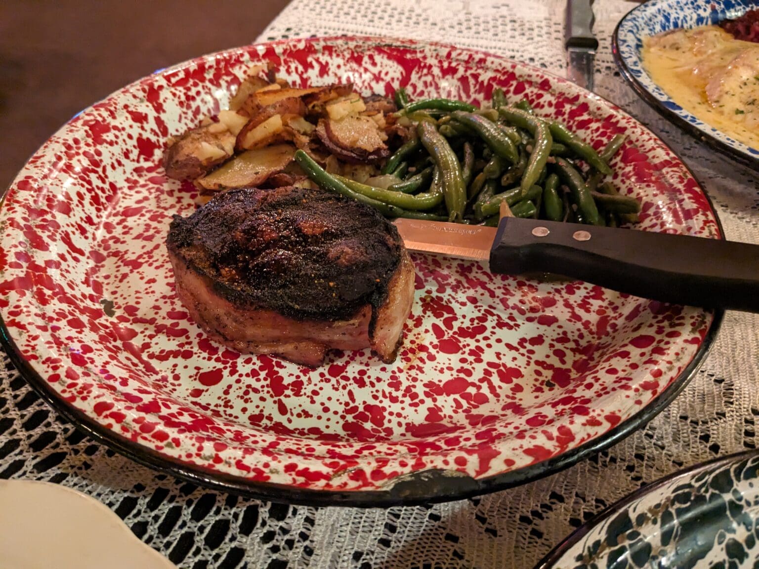 Bacon-wrapped filet mignon at Herb Niemann's Steak & Schnitzel House is served on a decorated red and white plate along with a steak knife.