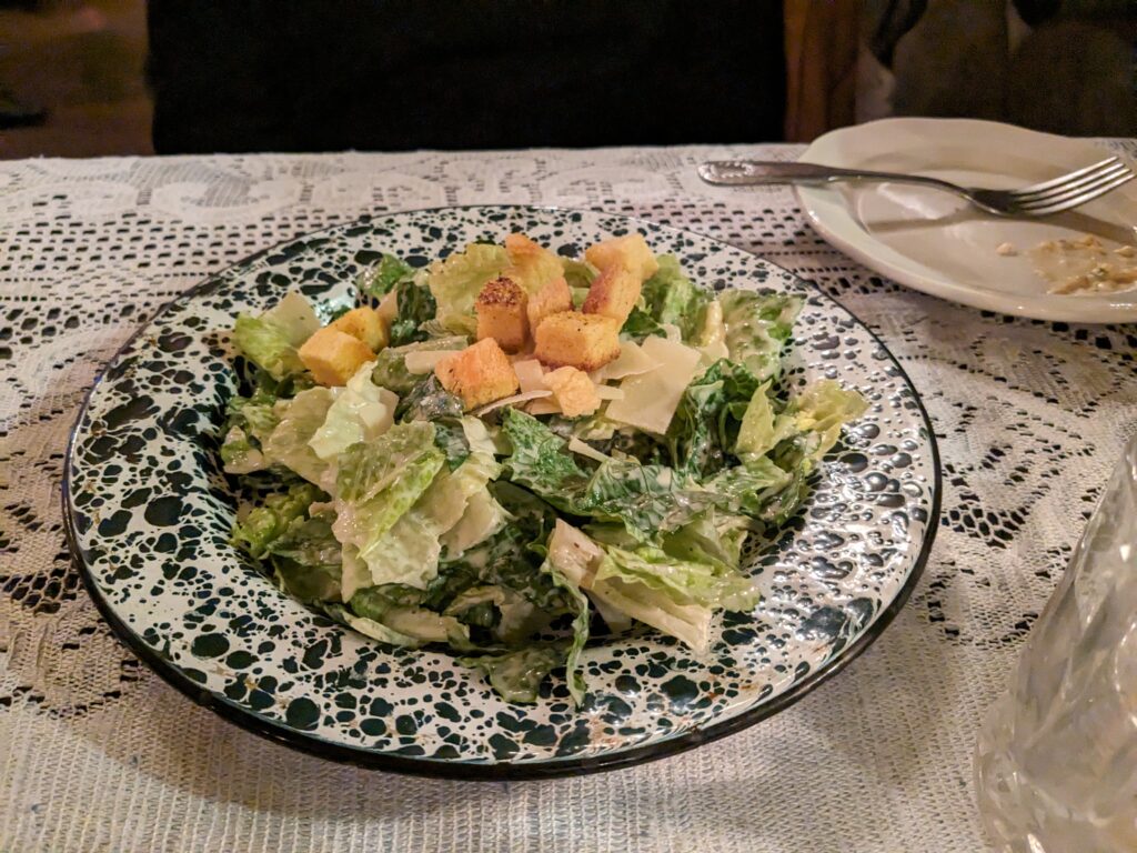 Caesar salad garnished with croutons and sharp cheese is served on a green and white plate.