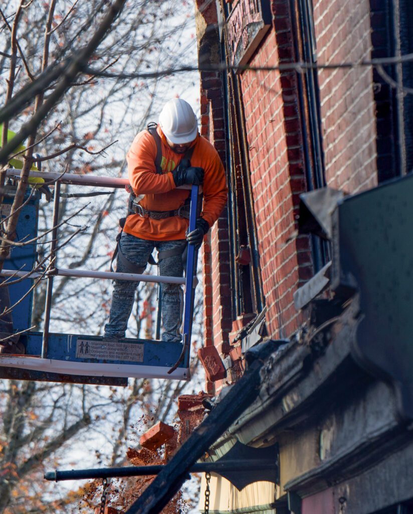 A worker uses priers to remove red bricks off the wall.