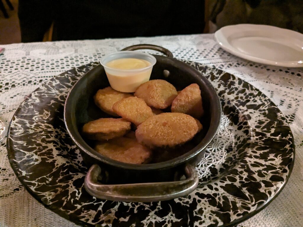 Breaded and deep fried zucchini is served in a small pot alongside a honey mustard dip.