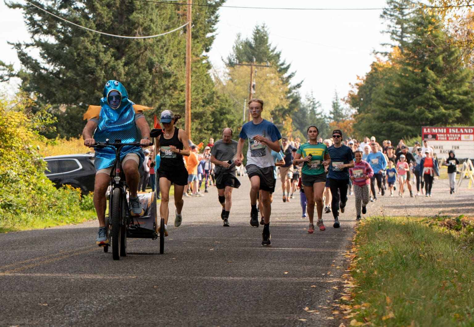 In a bright blue fish suit, Jesse Powell leads the 5k division on a bicycle.