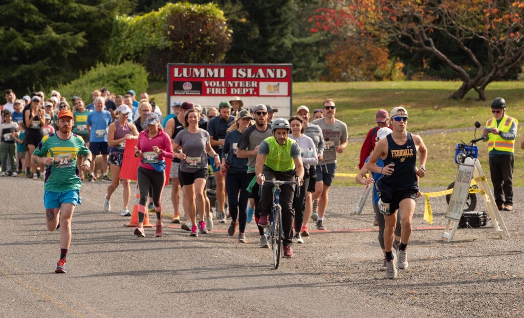 Runners behind and side by side with a person wearing a safety vest and riding a bicycle.