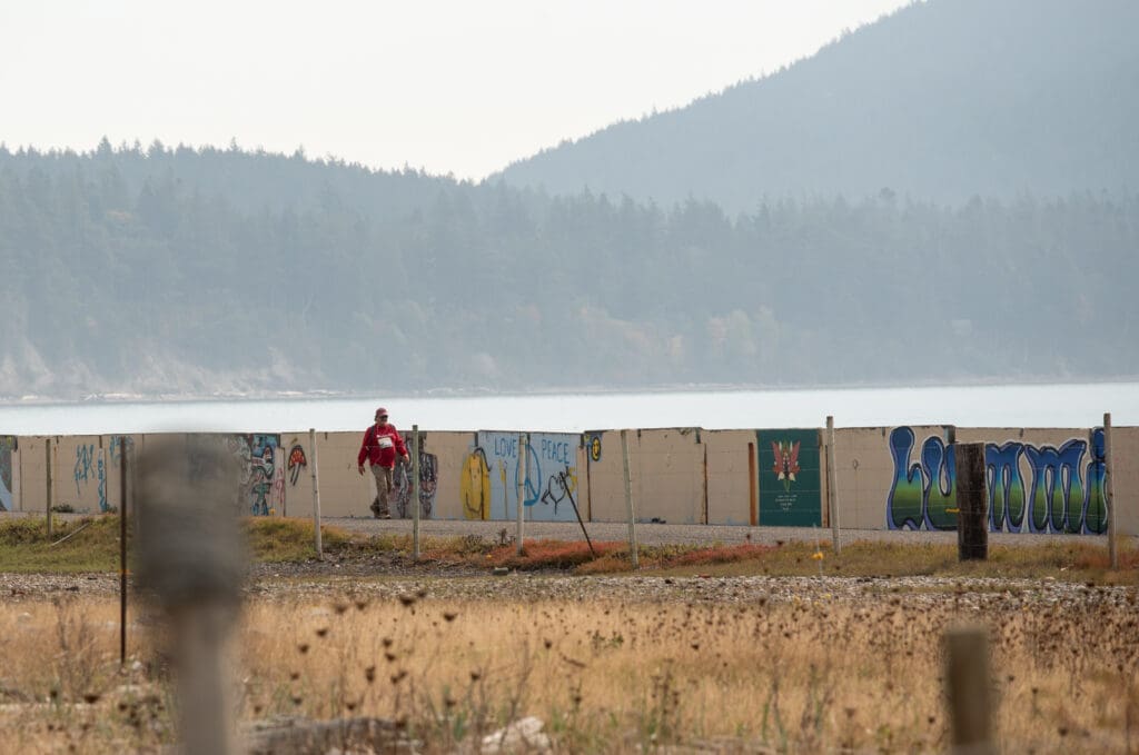 Steve Lurenz walks along Legoe Bay Road with the walls covered in grafitti next to him.