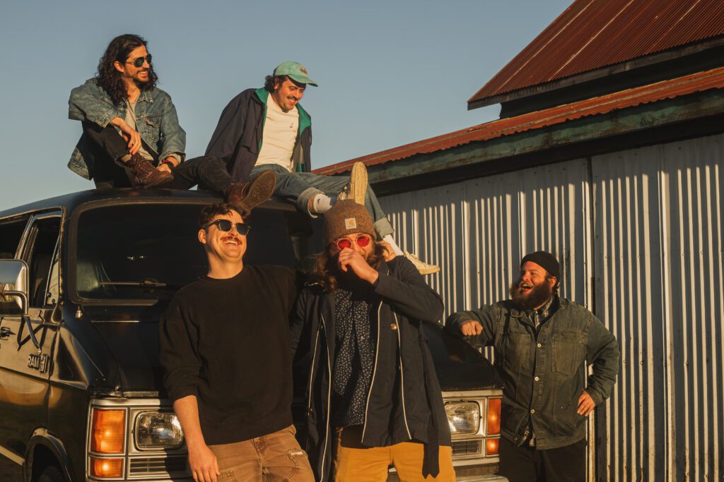 Smooth Kiwi laughs as they hang out at the van with two members sitting on the top of the van.