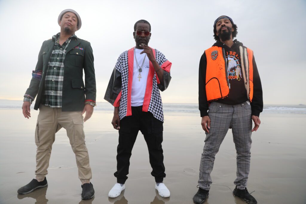 The Pharcyde poses for a photo on the beach, with one member holding a cigarette.