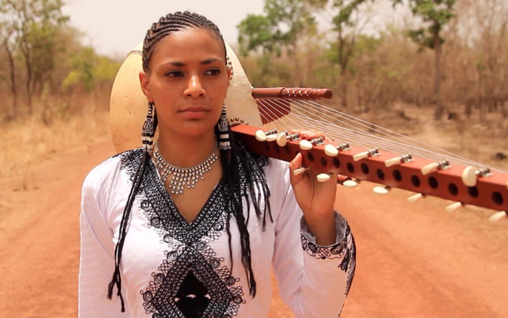 Sona Jobarteh holds up a string instrument with her shoulder.