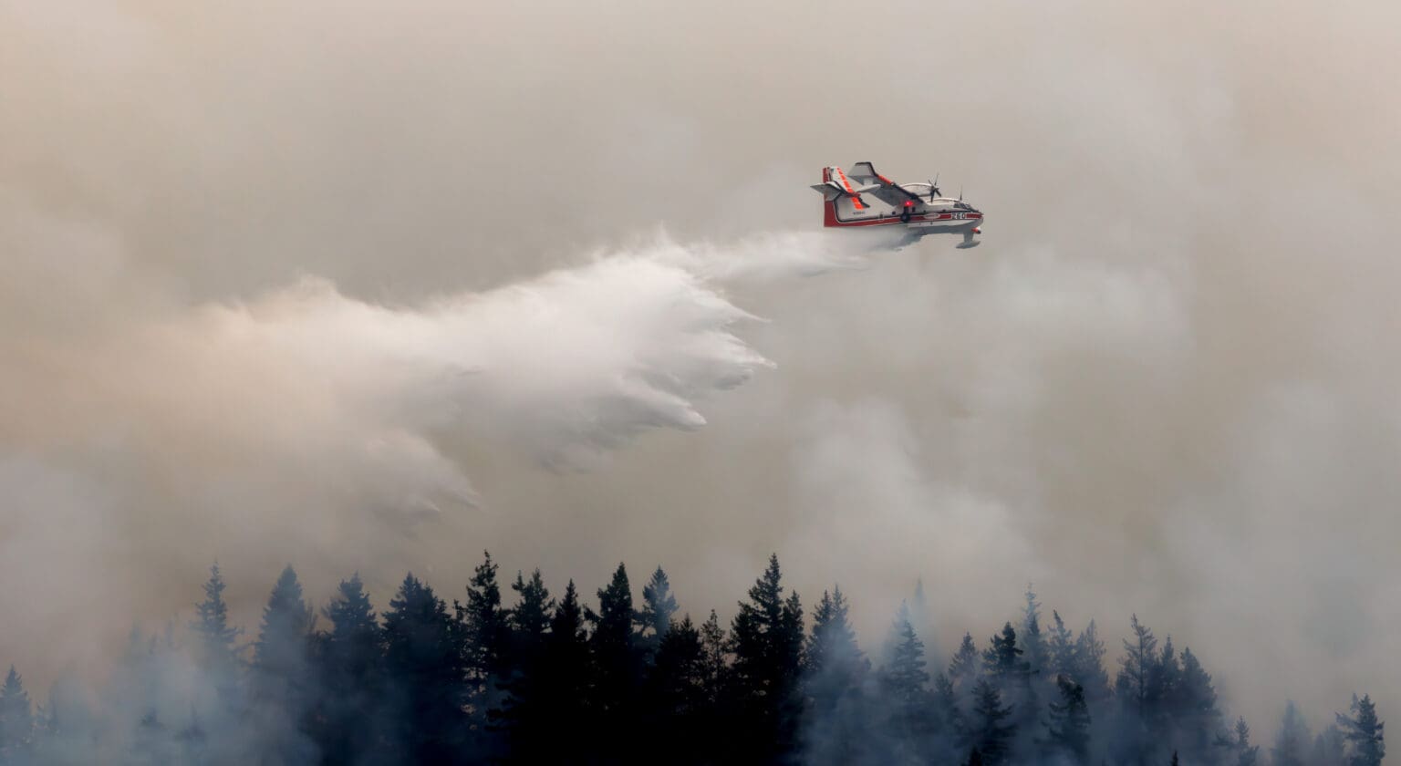 A scooper plane douses a wildfire on South Lake Whatcom from above as the sky is obscured by the smoke.