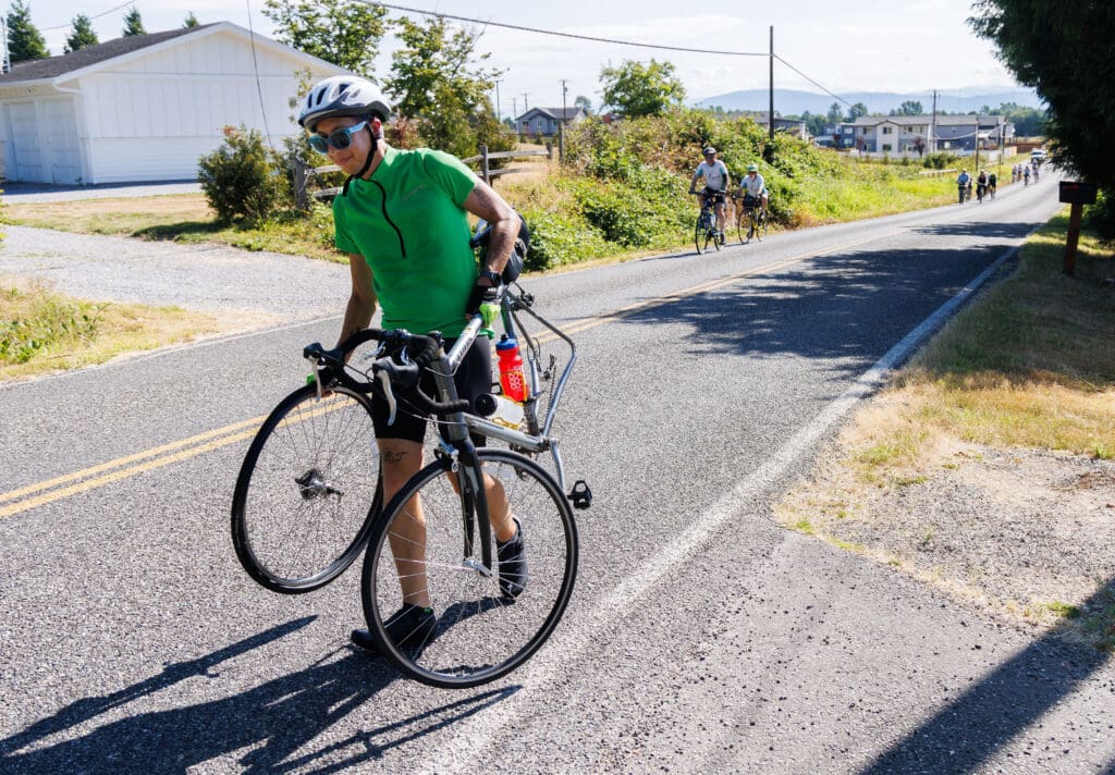 Suffering from a flat, James Sceshulte walks his bike and wheel to a nearby rest station during the Tour De Whatcom.