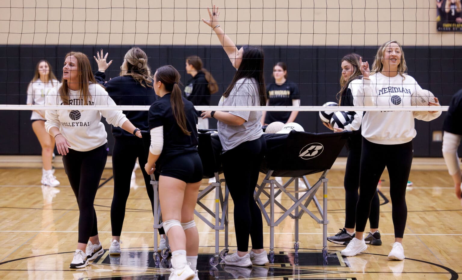 Meridian head coach Angie Short, left, and assistant coach Shannon Claeys run through drills next to a basket full of volleyballs.