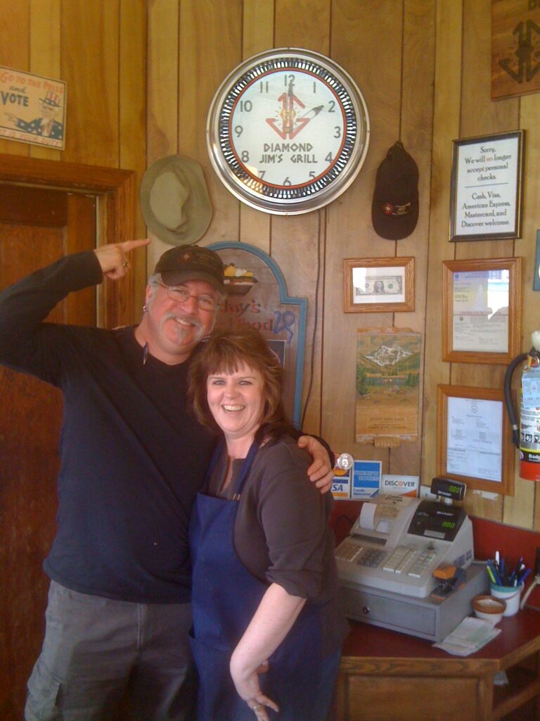 Jim Green, left, and longtime employee Sheryl Johnson pose for a picture with Jim Green pointing up to the clock that has a Diamond Jim's Grill theme.