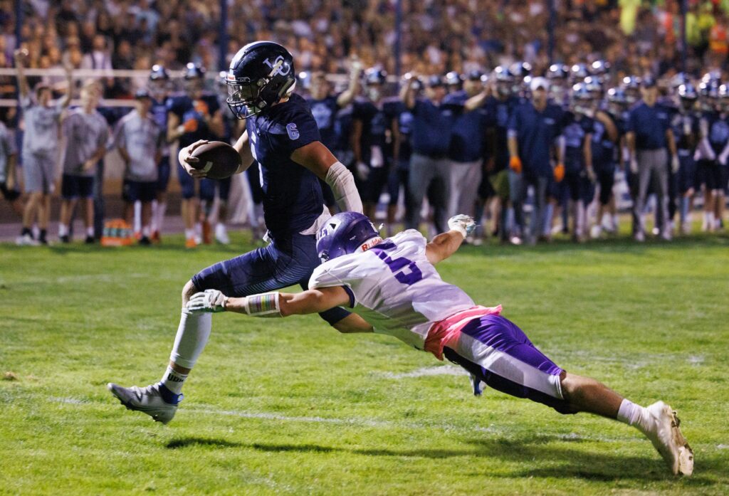 Jermiah Wright maneuvers to avoid a tackle from the opposing team's player as he dives with his arms spread while spectators on the sidelines watch on.