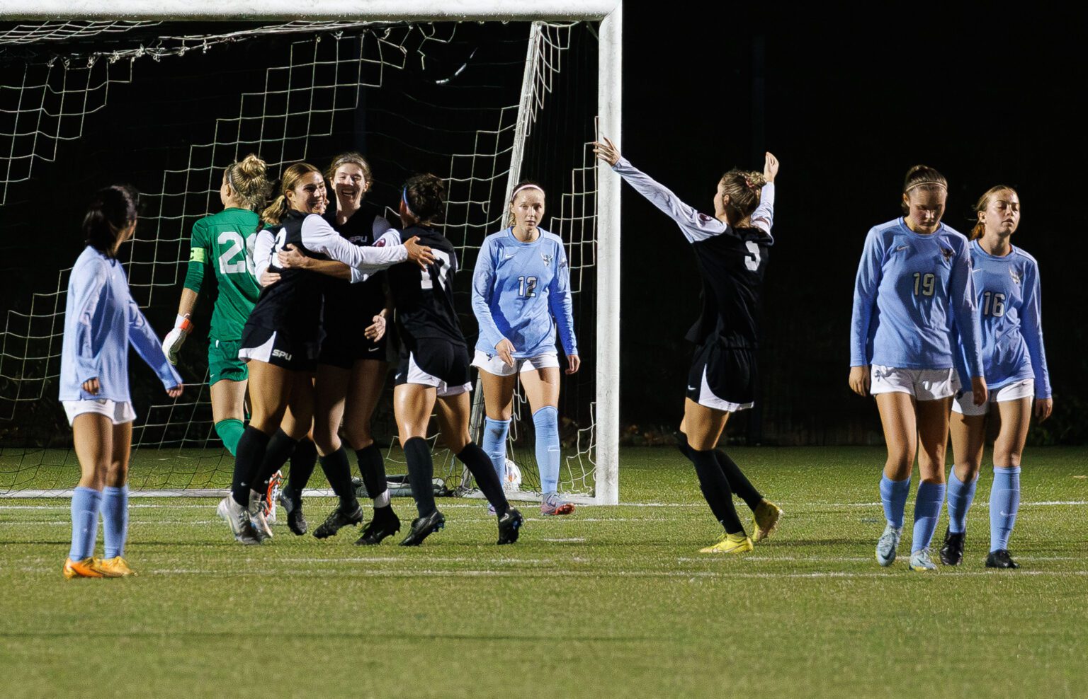 Seattle Pacific players celebrate a goal by hugging as another teammate joins them while other players walk away, defeated.