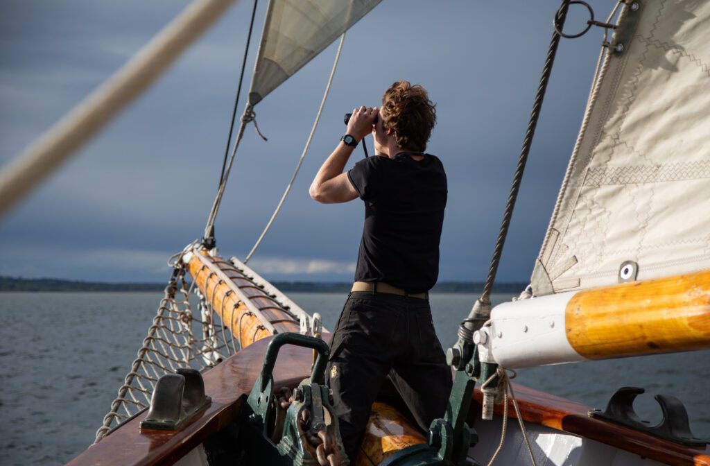 Intern Jackson Presley looks toward Lummi Island with binoculars from the bow of the ship.