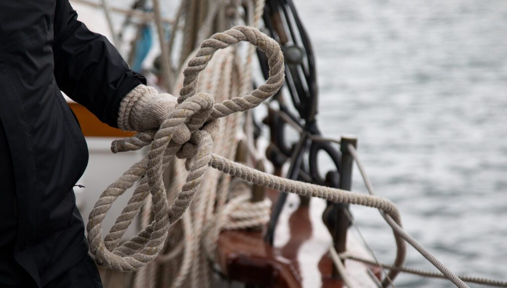 A crew member gathers a line while raising sails.