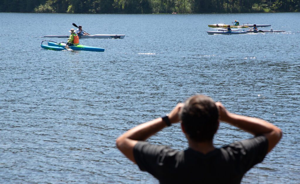 A spectator watches the elementary school kayak leg with binoculars.