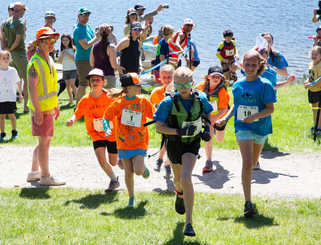 A.E.E.E.A! in orange and the Salish Sisters in blue run to the finish line.