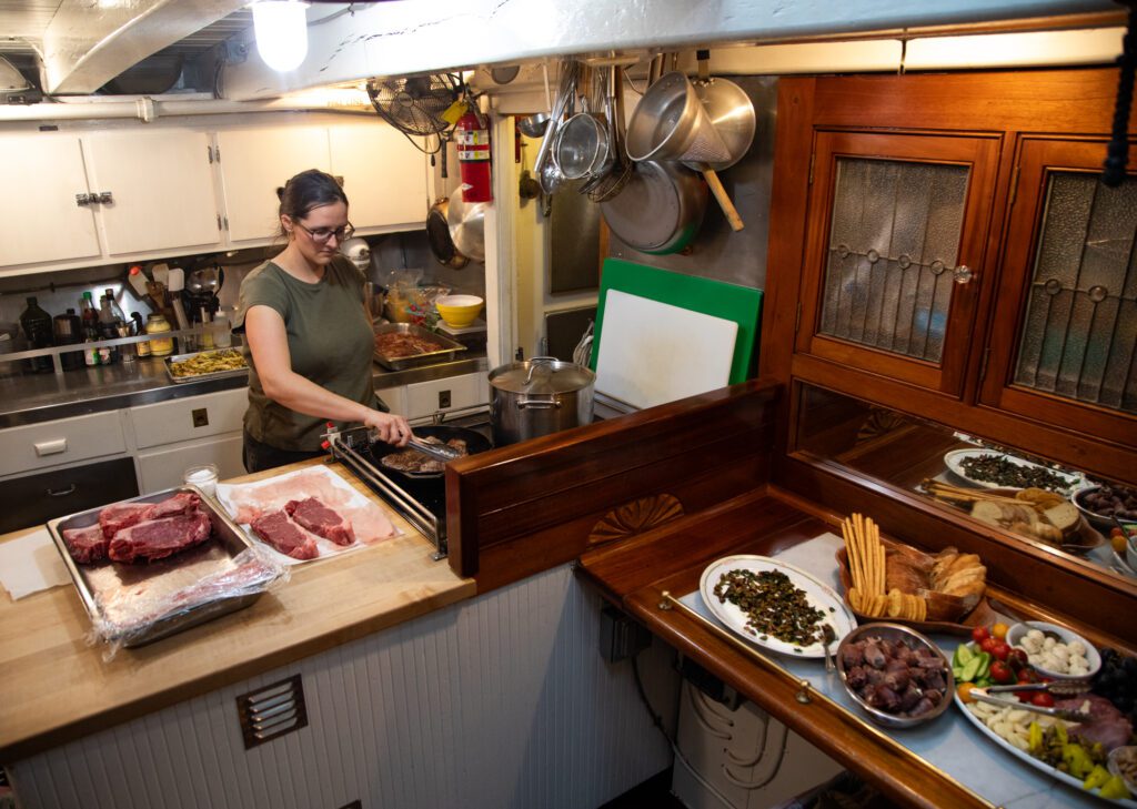 Cook Caz Ludtke cooks steaks in a pan for the main course meal after a round of appetizers. Ludtke has cooked on the vessel for about a decade, serving thousands of passengers with hearty salmon dinners and other delicious dishes.