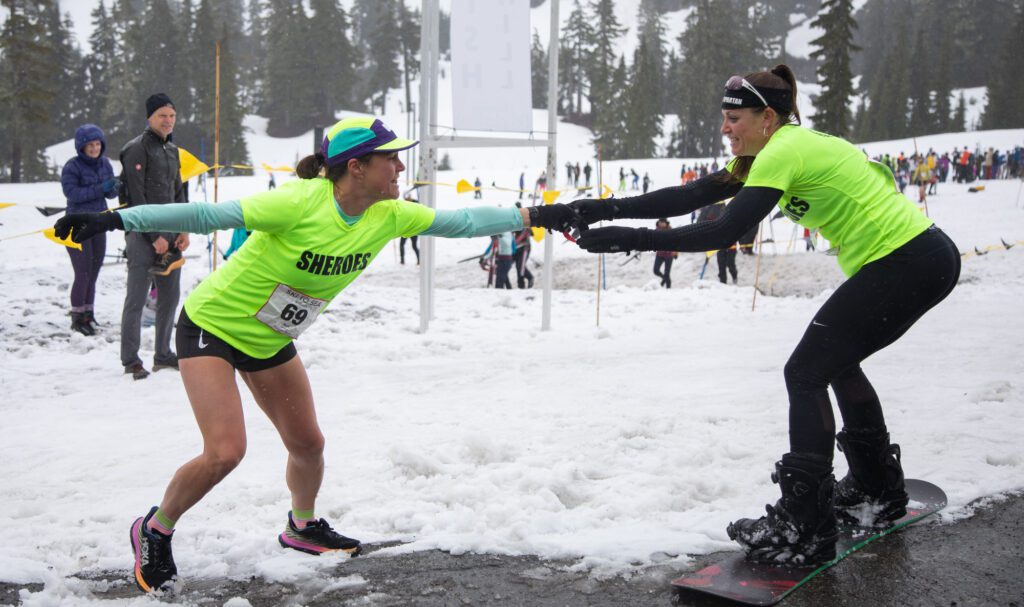 Snowboarder Alyson Carlyon Stewart of team Sheroes hands off to runner Aly Huerter after finishing the second leg in 28:59.2.