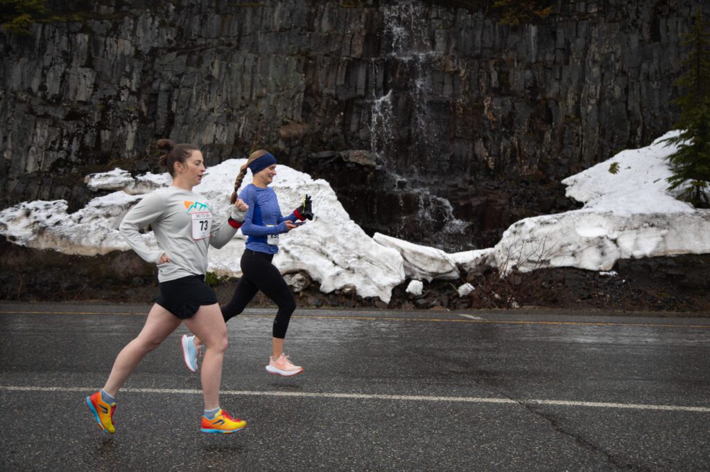 Kelsey Bracewell of team American Canoe Association Women, left, and Whitney Kiker of the Indie Gals & New England's Finest run past a waterfall on Highway 542. The wet conditions slowed runners down.