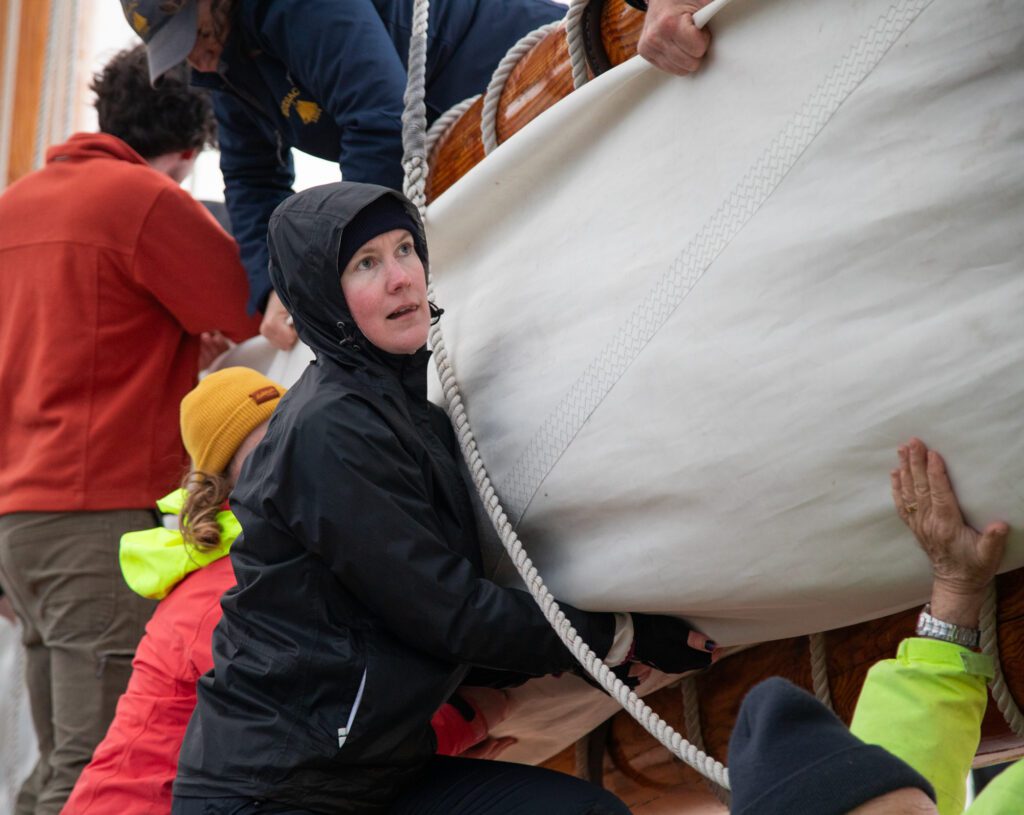 New volunteer crew member Cassie Lovert helps secure the foresail between the gaff and beam.