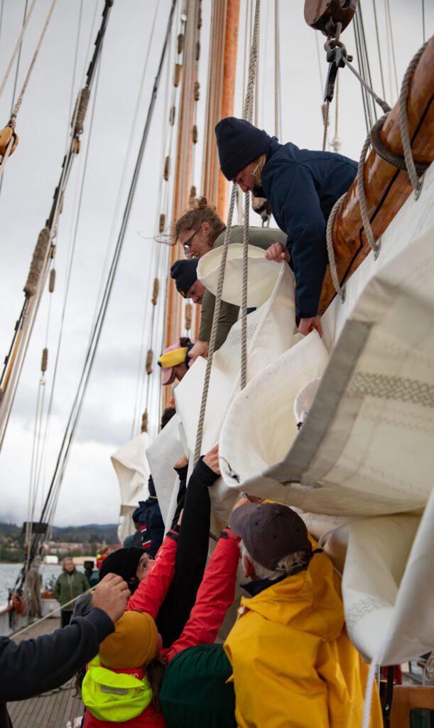 The crew stows away the new main sail during their training cruise. When a sail ends, it is secured between the gaff and the beam.