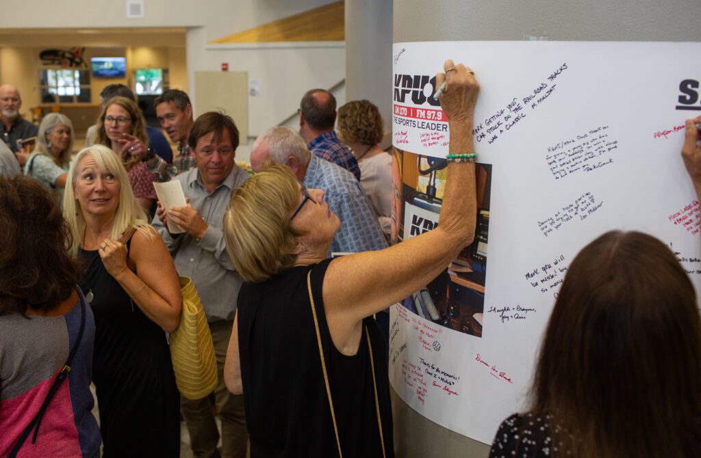 People write their memories of Mark Scholten on a poster taped on a column with a photo of him in the center.