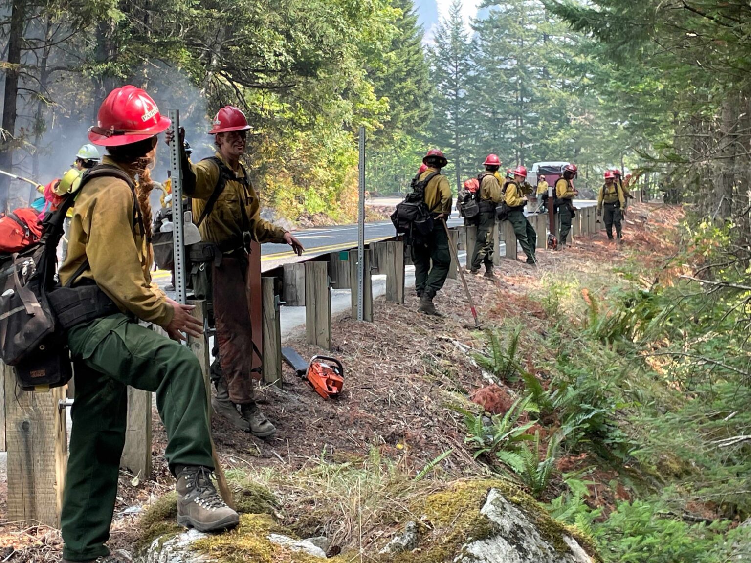 Firefighters rest and chat alongside the road with some having their faces covered in soot.