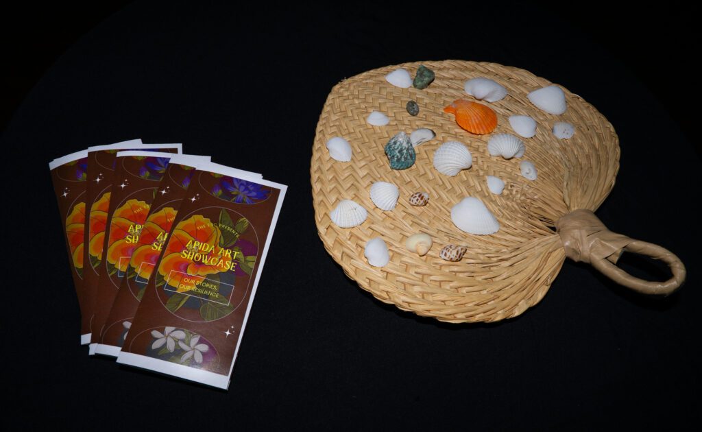 Shells and brochures rest on tables around the multipurpose room. The brochure cover was designed for the event by artist Susan Puailiau Lindsey.