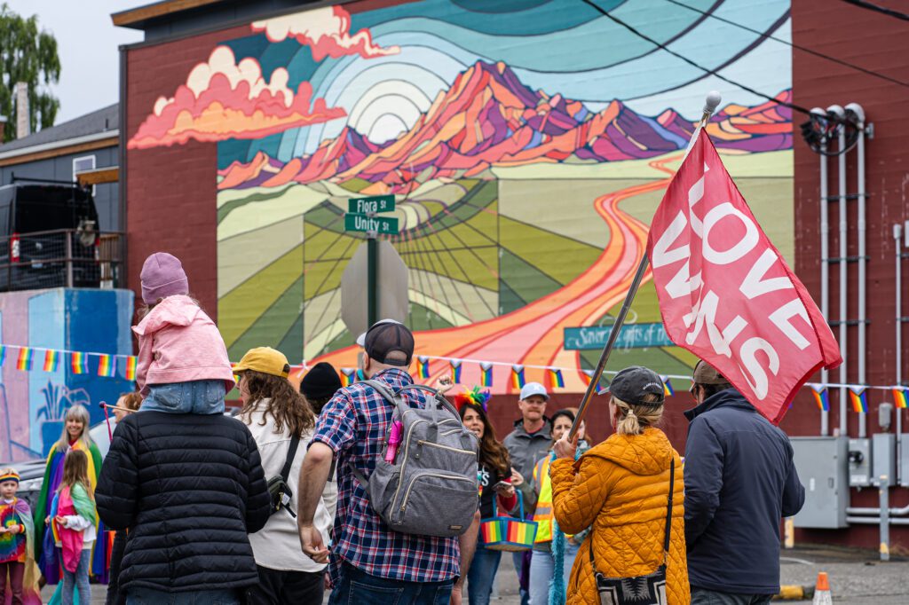 Parade members hold a flag stating "love wins" as they pass by a mural by Gretchen Leggitt in downtown Bellingham.