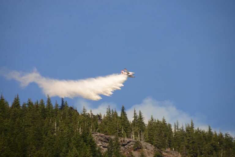 A plane flies by dropping gallons of water over the forest fire.