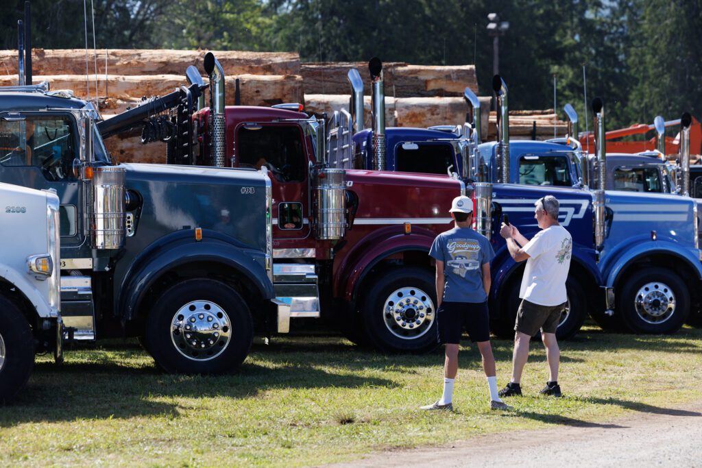 Spectators photograph logging trucks.