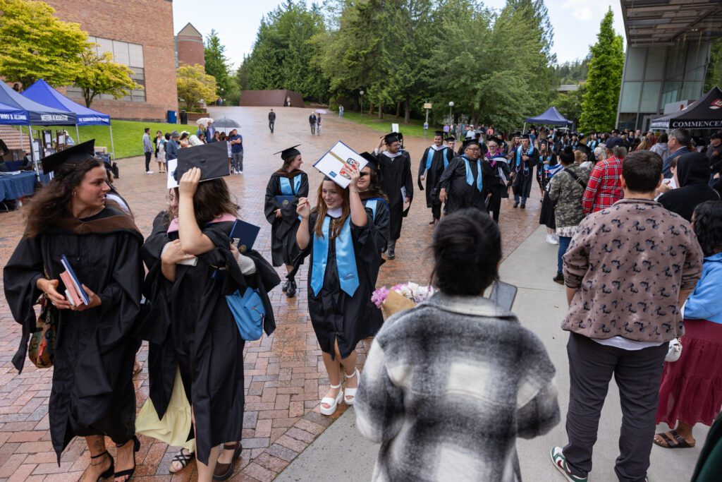 Graduates cover their heads from the rain as they depart Carver Gym.