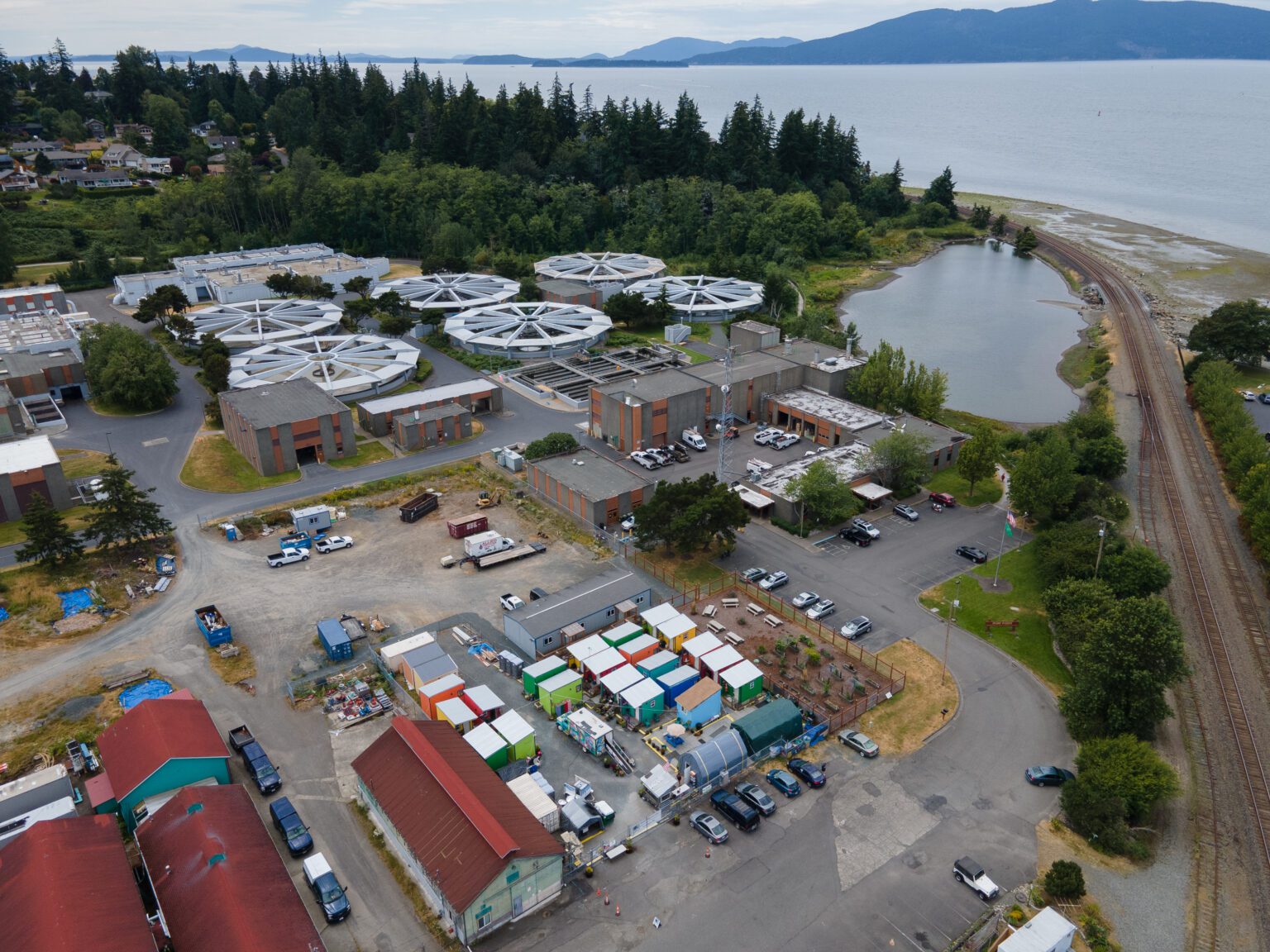 An aerial view of the Post Point Wastewater Treatment Plant has multiple small buildings near the waterfront.