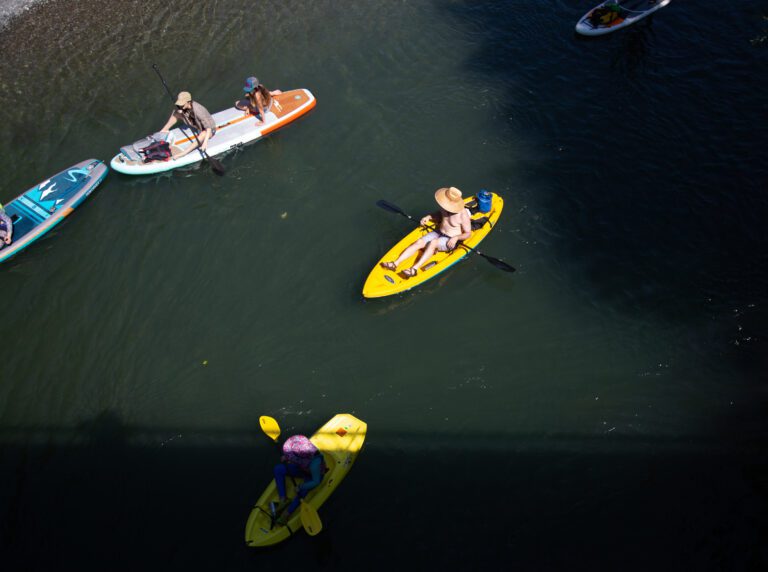 People in various colored kayaks paddle through the South Fork Nooksack River.