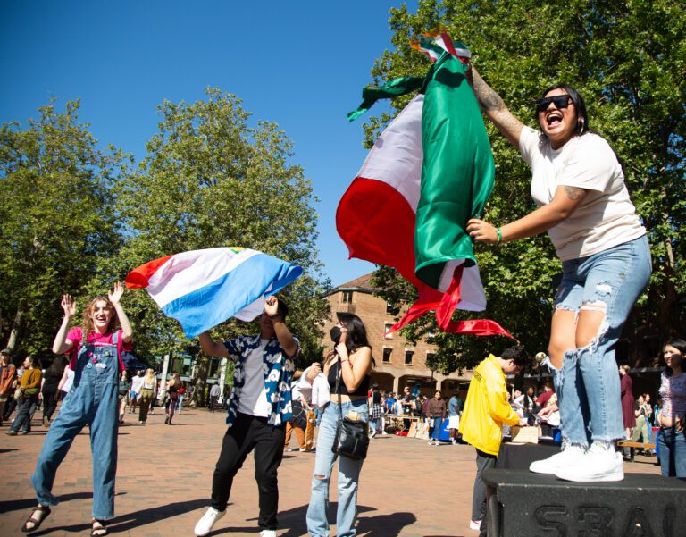 Yaileen Gonzalez waves the mexican flag on a podium as other students watch and wave their own flag as well.