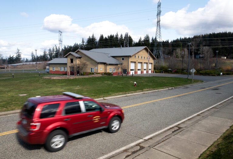 A red car drives by next to a fire station.