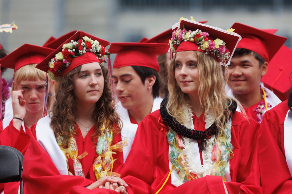 Elena Ficklin holds Maddie Miller’s hand as they listen to speakers at the Bellingham High School graduation ceremony.