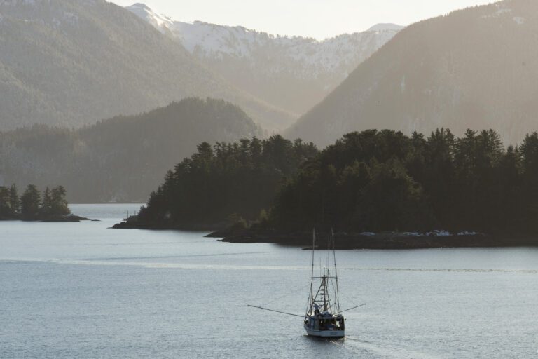 A troller fishes in Sitka Sound, Alaska, heads towards the forests surrounded by large mountains.