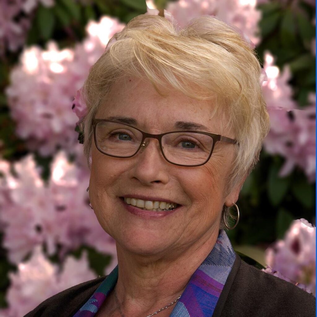 A woman wearing glasses with short hair in front of pink flowers