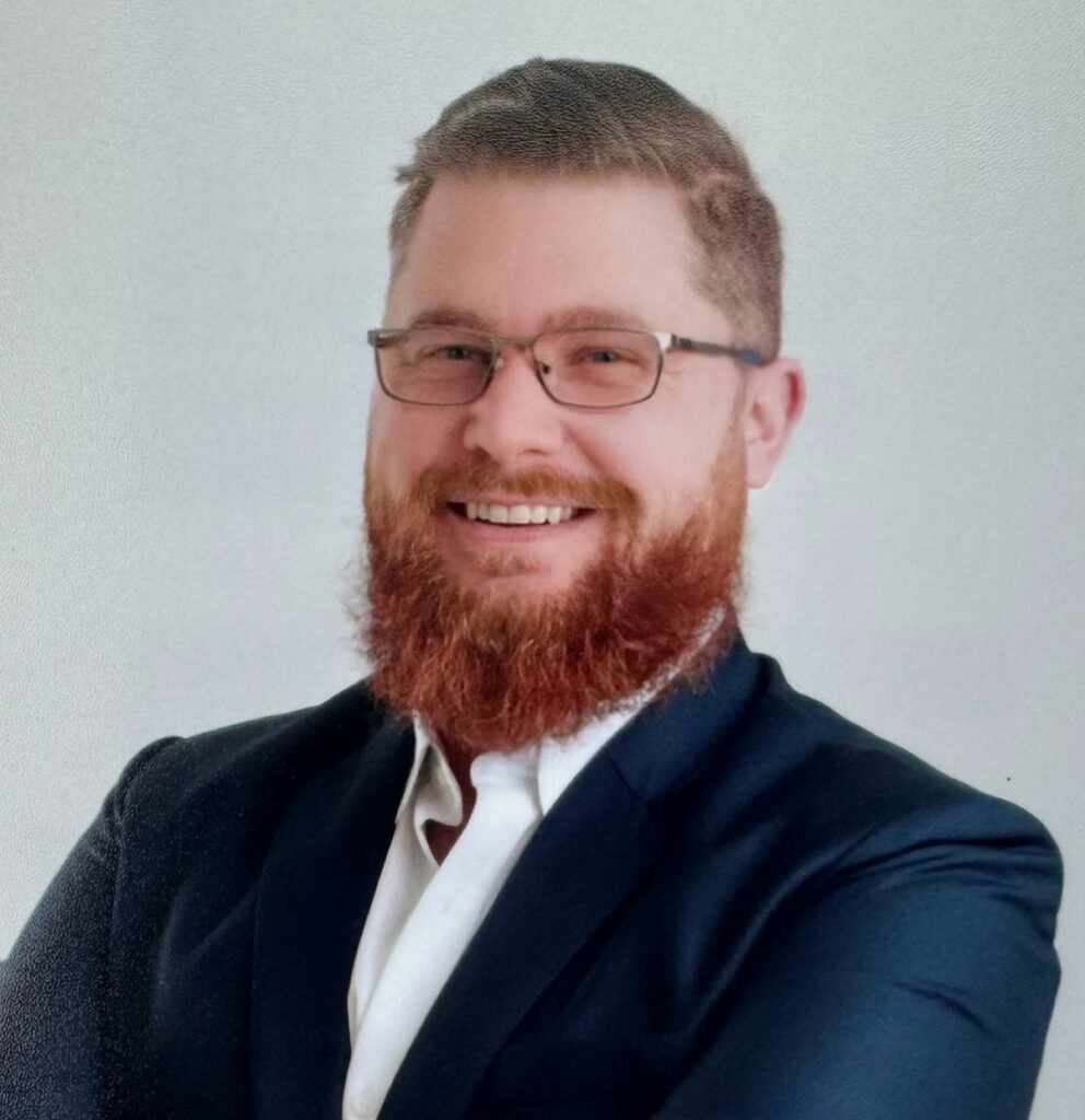 A man with a beard and glasses in a suit and tie.