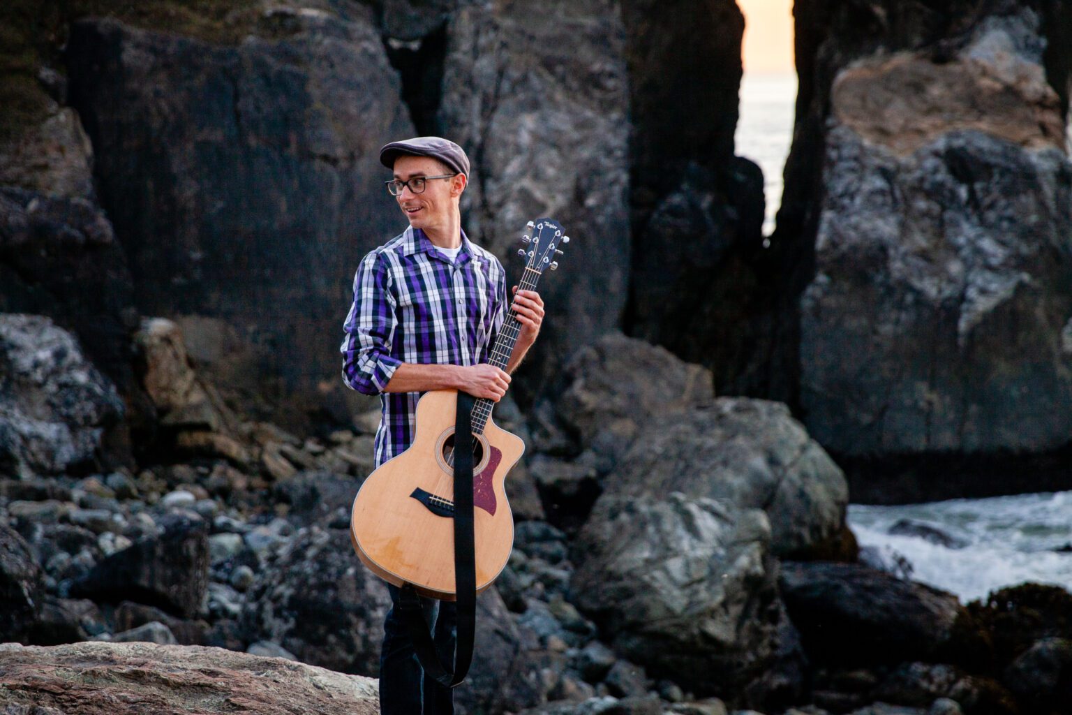 Area musician Michael Dayvid holds an acoustic guitar near the waters on the rocks.
