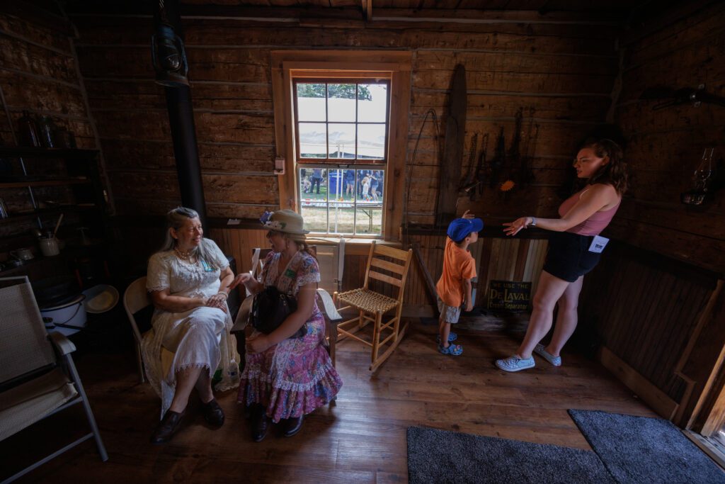 Volunteers Kay Sutcliffe, left, and Jerilyn Peterson chat Saturday, July 27 as Sidney Lavin, right, explains traps to Xavi Lavin at the Whatcom County Old Settlers Association's 128th Pioneer Days Celebration in Ferndale.