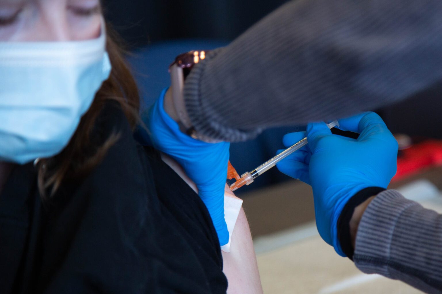 A healthcare professional administers a shot for a patient on their arm.